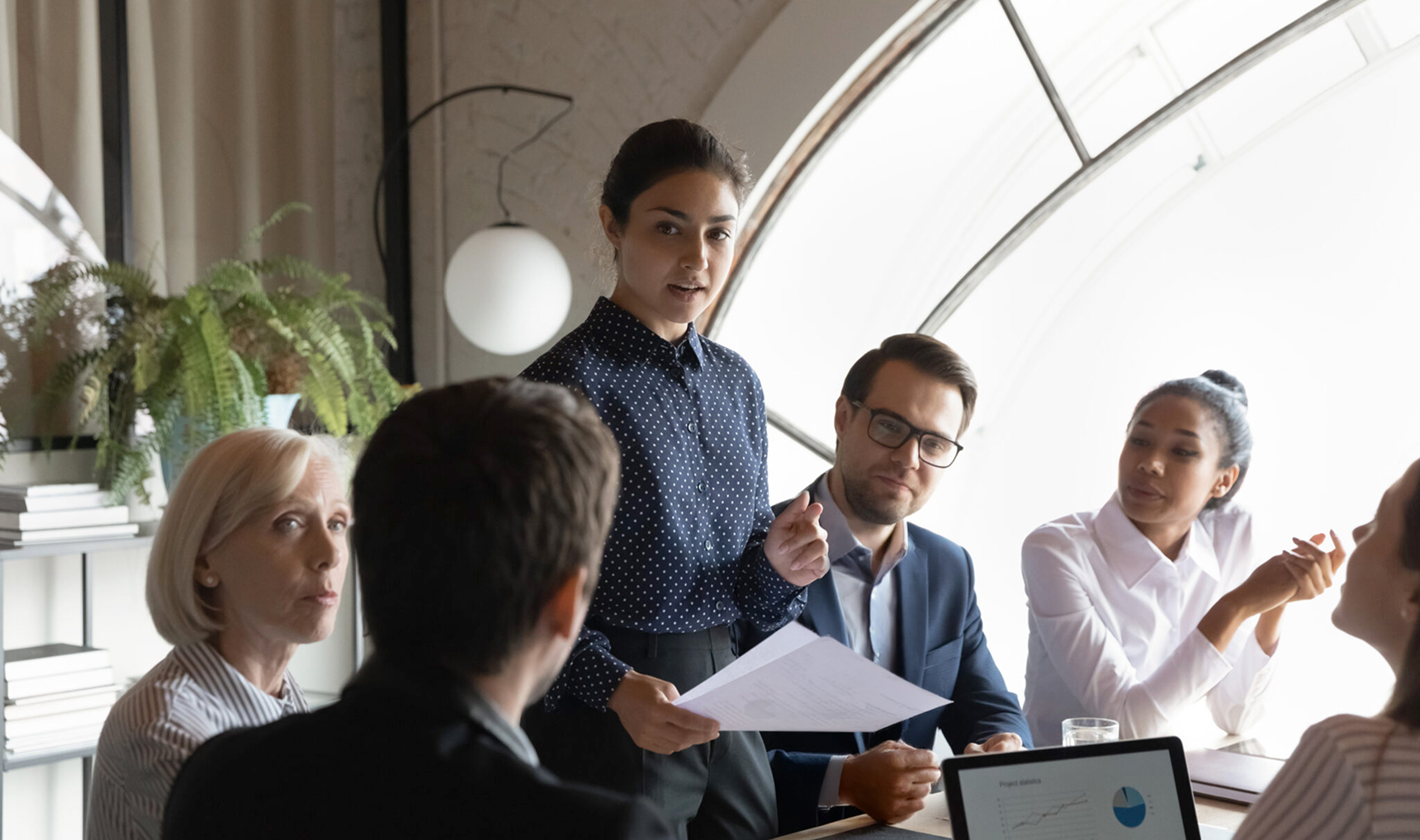 A woman standing in a conference room among her colleagues presenting